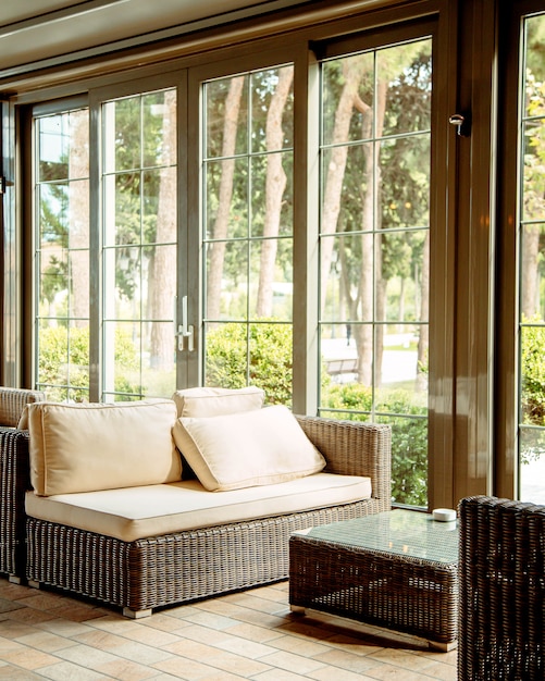 Canapé d'extérieur avec coussins beiges et table basse devant la fenêtre du restaurant