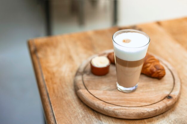 Cappuccino en verre avec croissant sur plateau circulaire en bois