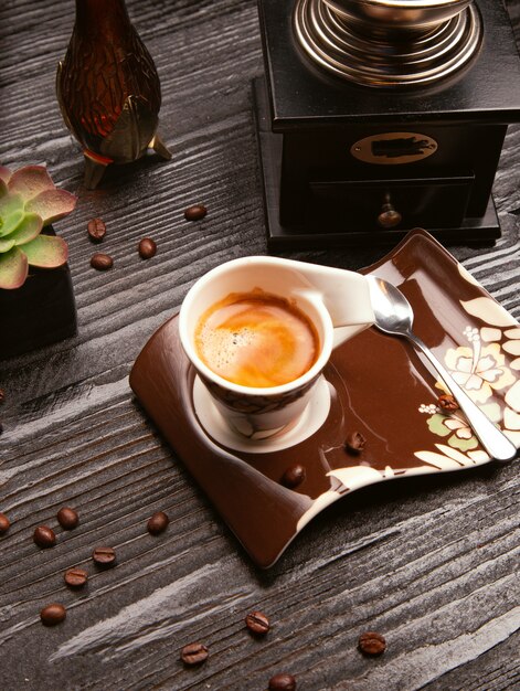 Cappuchino en mousse de lait, café au lait dans une tasse décorative et assiette marron avec une cuillère en métal.