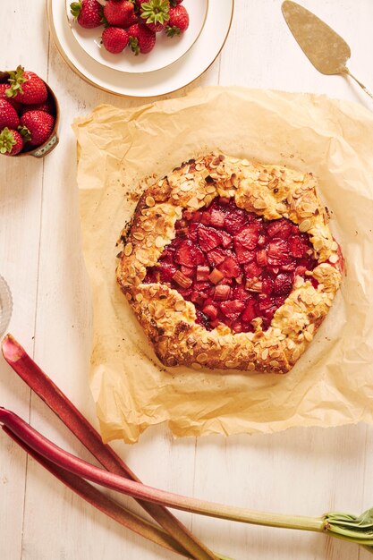 Capture en grand angle d'un délicieux gâteau au gallate de fraises à la rhubarbe avec des ingrédients sur une table blanche