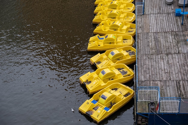 Capture en grand angle des pédalos jaunes fatigués de la jetée en bois sur la surface calme de l'eau