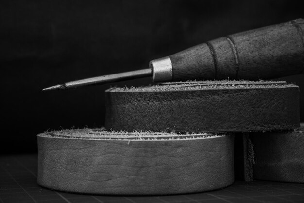 Capture en niveaux de gris d'un poinçon en bois et de rouleaux de cuir véritable sur une table de travail d'artisan