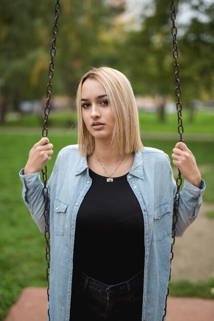 Capture verticale d'une belle femme caucasienne en denim tenant une balançoire en métal dans le parc