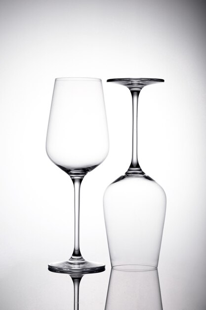 Capture verticale de deux verres à vin vides sur la surface blanche avec des ombres, l'un est à l'envers
