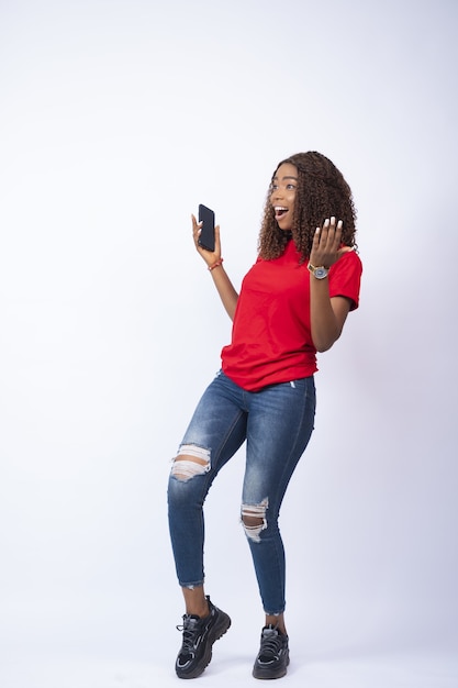 Photo gratuite capture verticale d'une jeune femme africaine excitée tenant son téléphone regardant joyeusement vers son côté