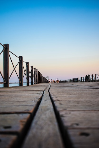 Photo gratuite capture verticale d'un quai en bois entouré de clôtures sous le ciel bleu le soir