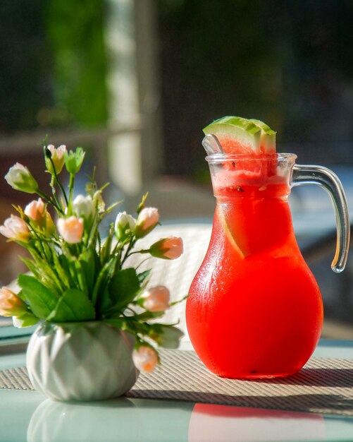 Carafe avec du jus de pastèque froid et un vase de fleurs