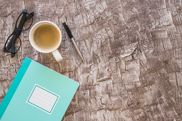 Carnet; tasse à café; lunettes et stylo sur fond texturé