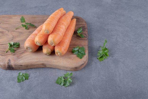 Carottes crues avec des verts sur la planche à découper, sur la surface en marbre.