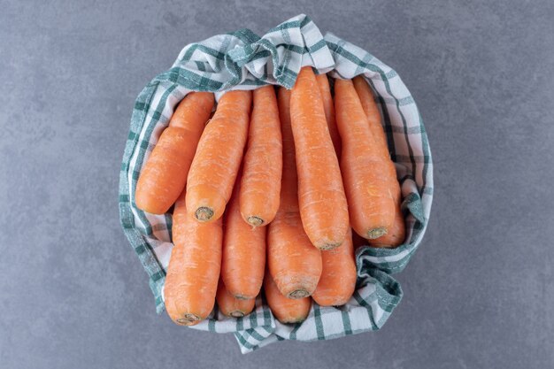 Carottes fraîches sur une serviette dans le bol, sur la surface en marbre.