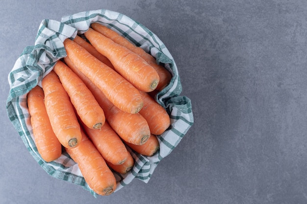 Carottes fraîches sur une serviette dans le bol, sur la surface en marbre.