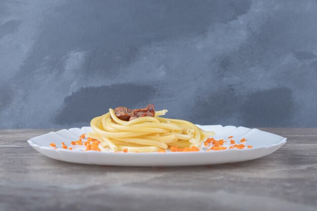 Photo gratuite carottes râpées et spaghettis à la viande sur l'assiette, sur la surface en marbre.