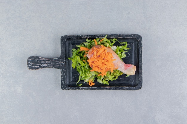 Carottes savoureuses et verts avec cuisse de poulet sur la planche, sur la surface blanche