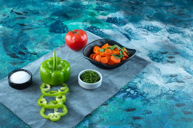 Carottes tranchées dans un bol à côté de légumes sur une serviette , sur la table bleue.