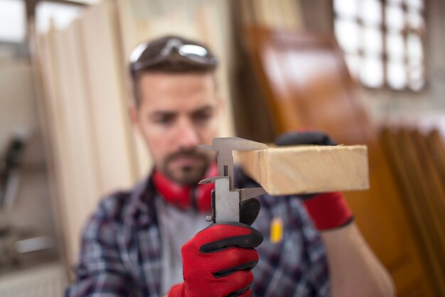 Carpenter mesurant l'épaisseur du matériau en bois de planche avec pied à coulisse pour un nouveau projet