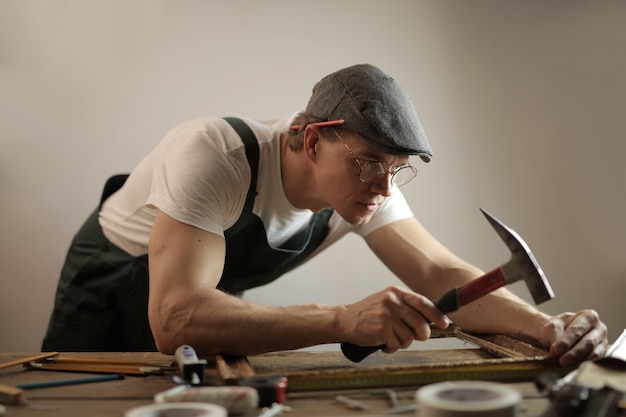Carpenter portant un casque blanc travaillant avec un marteau et des vis essayant de fixer une table en bois