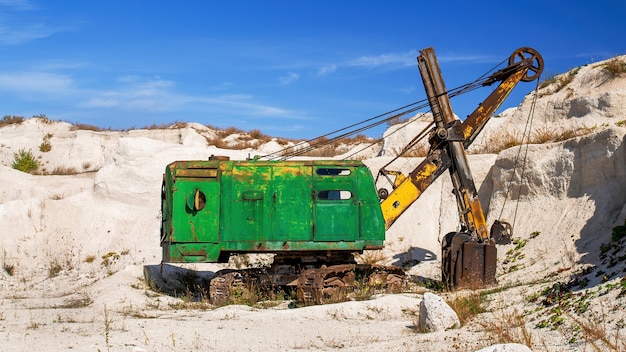 Carrière de calcaire avec une végétation clairsemée et ancienne excavatrice abandonnée et rouillée