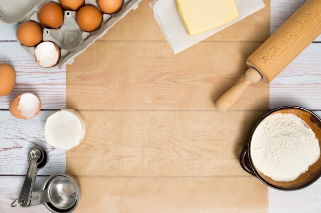 Carton d&#39;oeufs; beurre; rouleau à pâtisserie; farine et cuillère à mesurer sur une table en bois