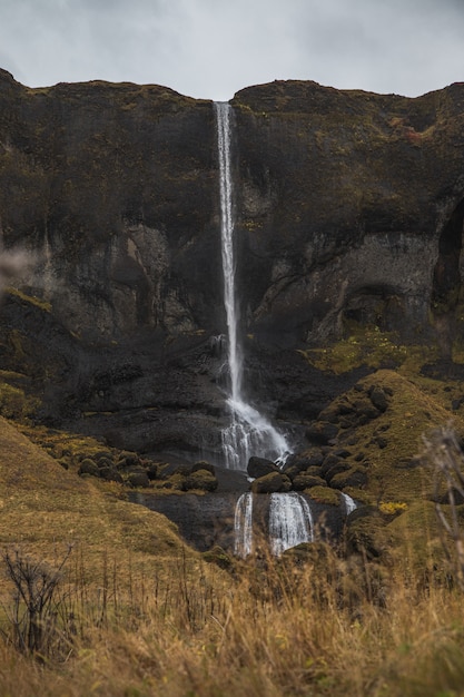 Photo gratuite cascade entourée de rochers et d'herbe sèche sous un ciel nuageux