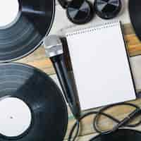 Photo gratuite casque de musique; microphone; disque vinyle et bloc-notes à spirale vierge sur une table en bois