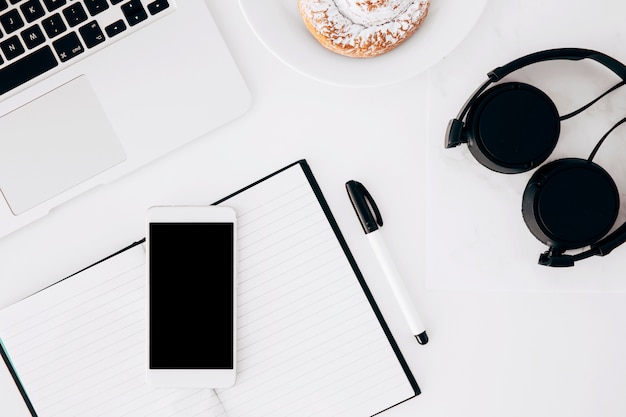 Casque de musique; portable; téléphone portable; journal intime; stylo et aliments cuits au four sur fond blanc