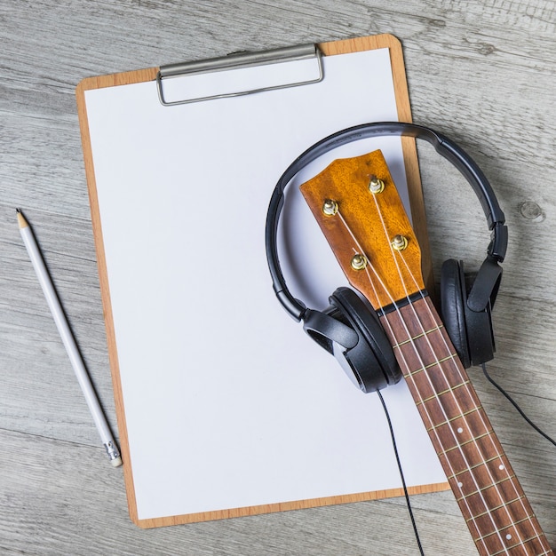 Photo gratuite casque sur la poupée de guitare sur le papier blanc sur le presse-papiers avec un crayon