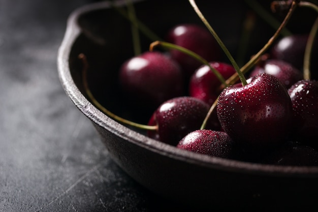 Casserole avec cerises sur une table en bois noir