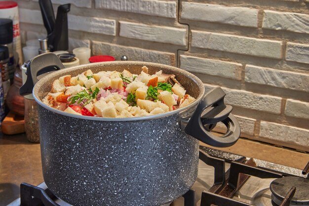Casserole sur la cuisinière à gaz avec des légumes pour la soupe et des morceaux de baguette.