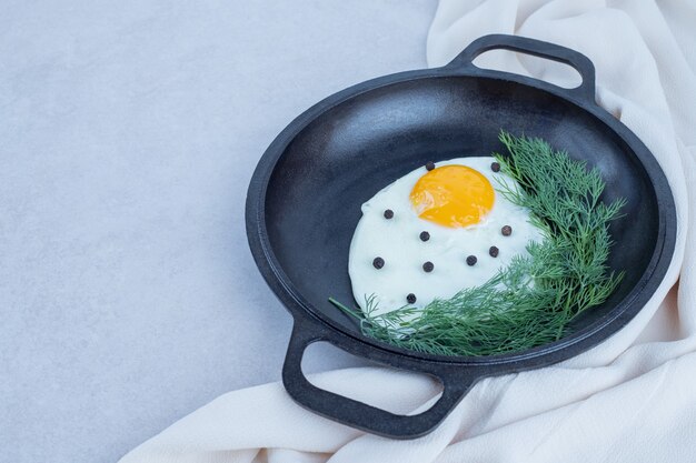 Une casserole d'omelette avec du poivre et des verts sur blanc.