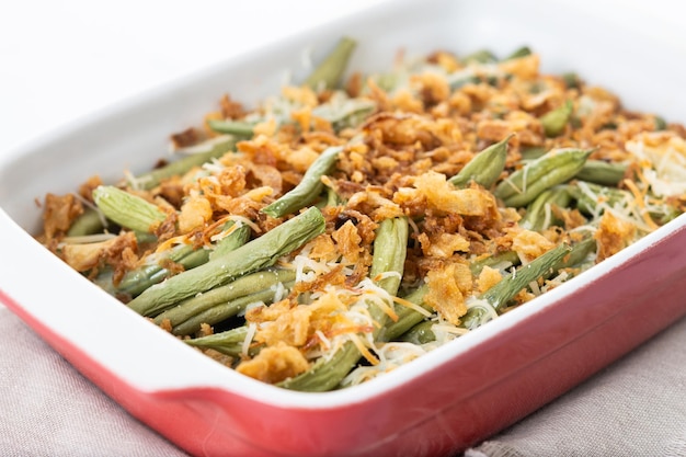 Une casserole traditionnelle de haricots verts surmontée d'oignons frits français et de crème de champignon isolée sur un fond blanc.