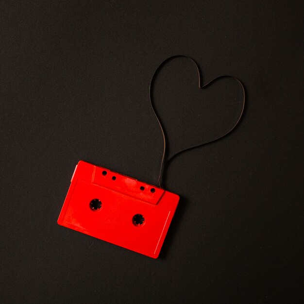 Cassette audio rouge avec bande magnétique en forme de coeur sur fond noir