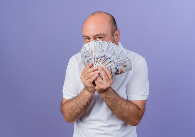 Casual homme d'affaires mature tenant de l'argent et regardant la caméra derrière l'argent isolé sur fond violet avec espace copie