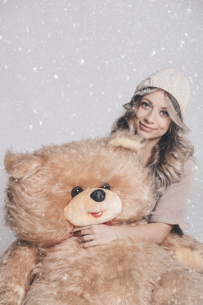 Casual jeune femme souriante dans des vêtements tricotés tenant un gros ours en peluche doux sur fond neigeux