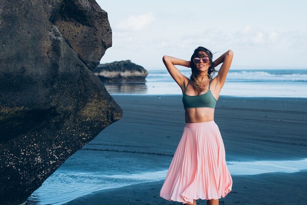 Caucasian fit femme bronzée en petit haut et jupe rose sur la plage de sable noir