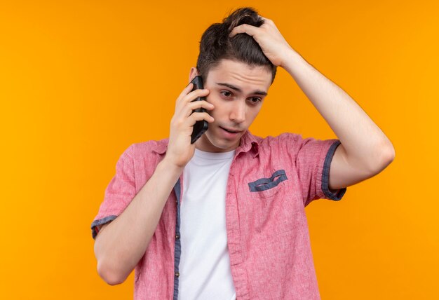 Caucasian young man wearing pink shirt spekeas on phone a saisi la tête sur un mur orange isolé