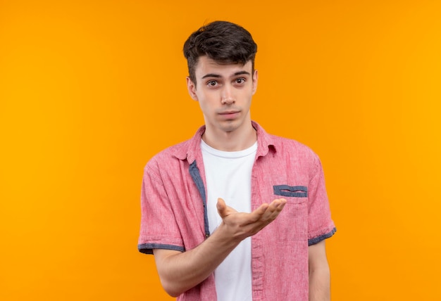 Caucasian young man wearing pink shirt tendit la main sur un mur orange isolé