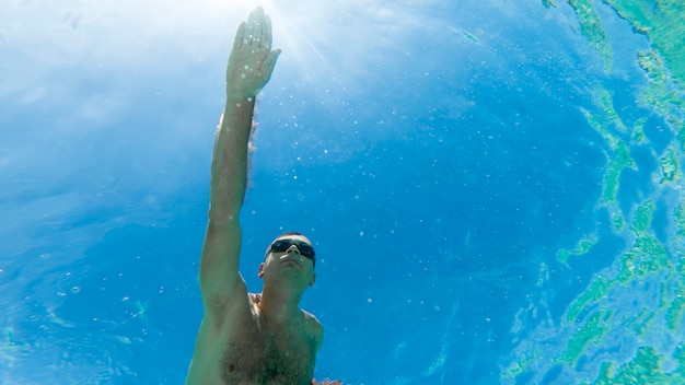 Caucasien homme nager sous l'eau dans des lunettes de natation bleu eau transparente