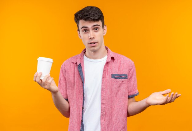 Caucasien jeune homme portant une chemise rose tenant une tasse de café montrant quel geste sur un mur orange isolé