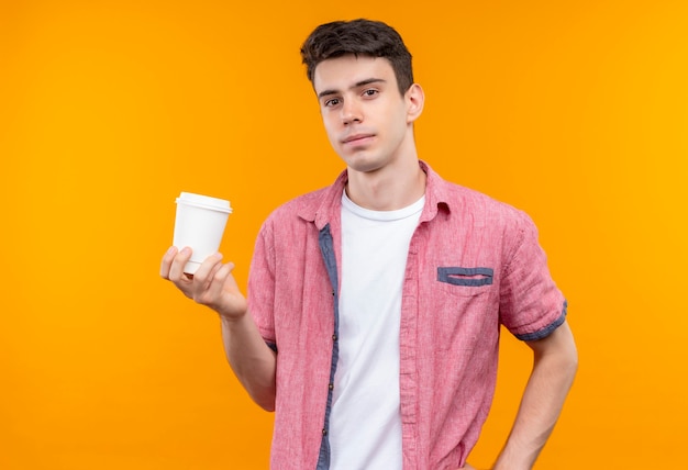 Caucasien jeune homme portant une chemise rose tenant une tasse de café sur un mur orange isolé