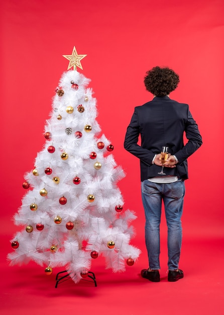 Célébration du nouvel an avec jeune homme tenant un verre de vin derrière un arbre de Noël blanc décoré