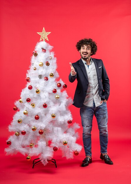 Célébration de Noël avec heureux jeune homme drôle accueillant quelqu'un debout près de l'arbre de Noël