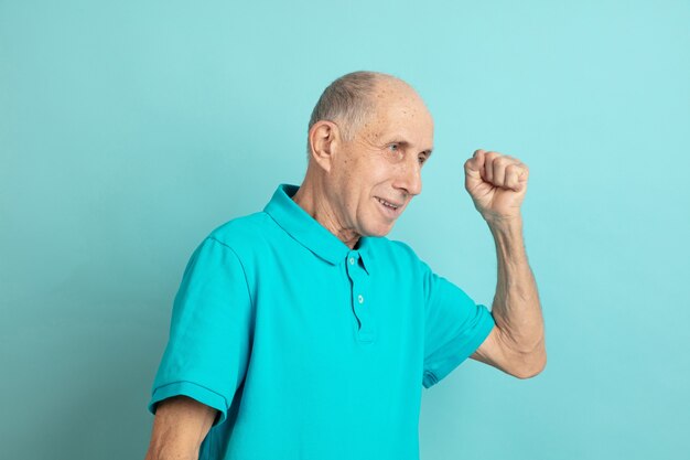 Célébrer la victoire, confiant. Portrait d'homme senior caucasien sur studio bleu.
