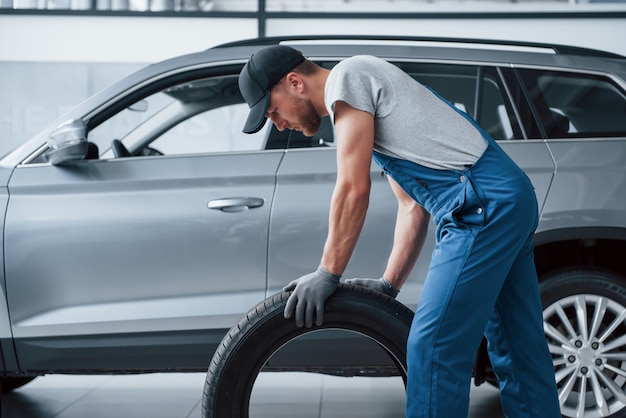 Celui-ci doit s'adapter parfaitement. Mécanicien tenant un pneu au garage de réparation. Remplacement des pneus d'hiver et d'été