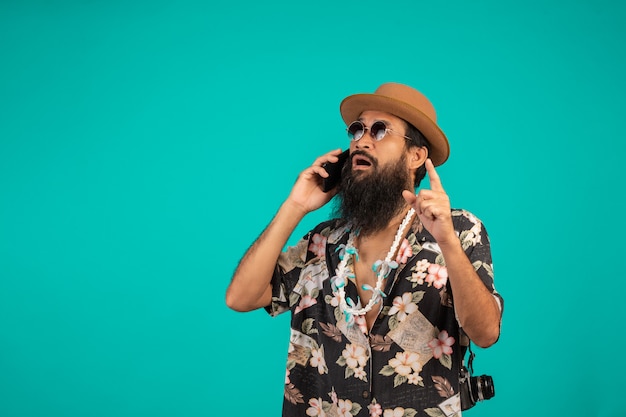 Celui d'un homme heureux à la longue barbe coiffé d'un chapeau, vêtu d'une chemise à rayures, tenant un téléphone sur un fond bleu.