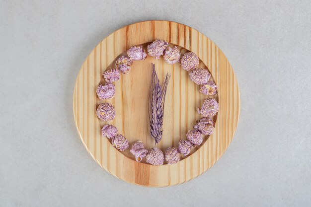 Cercle de bonbons de maïs soufflé sur une plaque en bois avec une tige de blé au milieu sur une table en marbre.