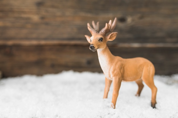 Photo gratuite cerf jouet sur la neige près du mur en bois