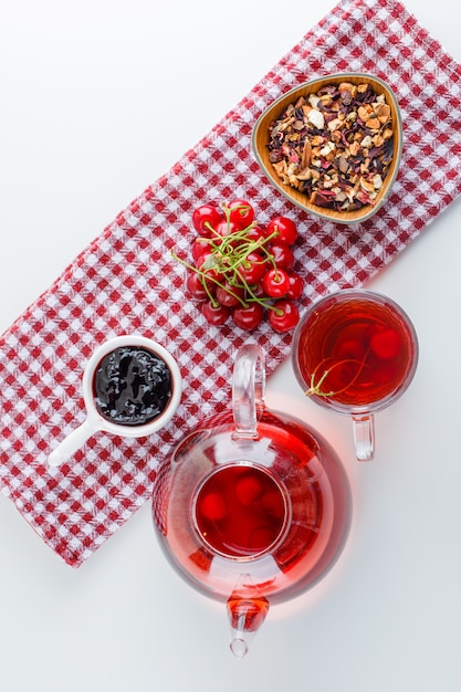 Cerise au thé, confiture, herbes séchées sur torchon blanc et cuisine, vue de dessus.