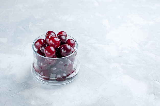 Cerises aigres fraîches à l'intérieur d'une petite tasse en verre sur un bureau à lumière blanche