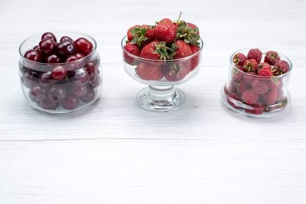 Cerises aigres rouges fraîches entières et moelleuses avec des fraises et des framboises sur un bureau léger