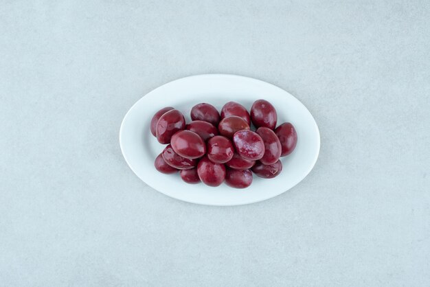 Cerises cornichons marinés sur plaque blanche.